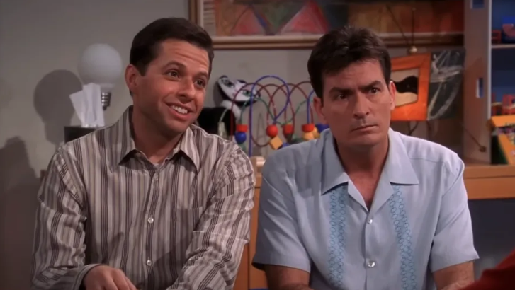 Charlie is sitting on a couch next to Alan Harper, with a slightly annoyed expression on his face.