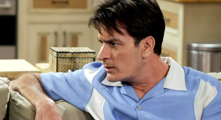Charlie is sitting on a couch, wearing a blue and white shirt and looking to the side with a serious expression.