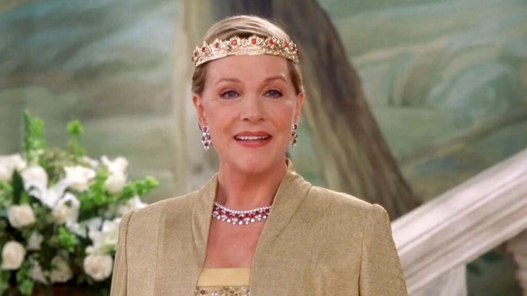Julie Andrews as Queen Clarisse Renaldi in The Princess Diaries 2: Royal Engagement woman wearing an ornate golden crown with red jewels and matching jewelry, dressed in royal gown.