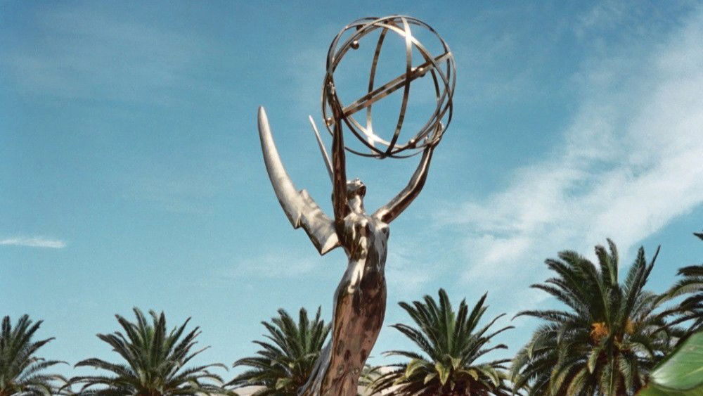A golden Emmy Award statue against a blue sky with palm trees in the background.