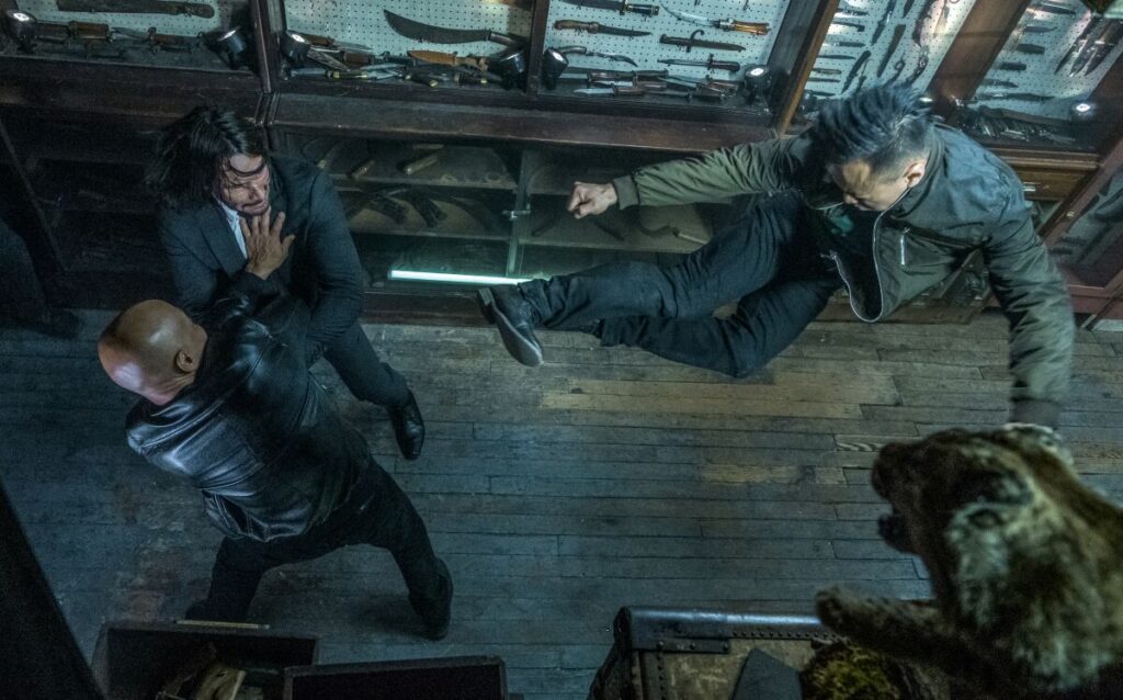 A man about to kick John Wick while the other holds him against the wall in John Wick: Chapter 3 - 
Parabellum