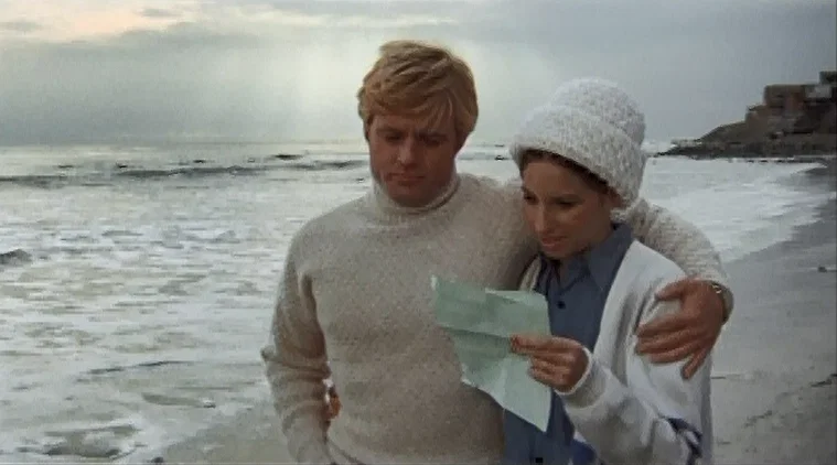 Barbra Streisand and Robert Redford walking on the beach reading a letter in The Way We Were