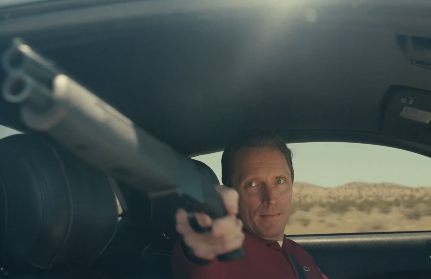 A man holding out a gun from a car in One Battle After Another. 