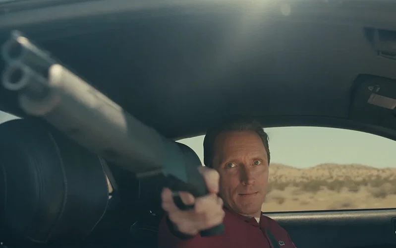 A man holding out a gun from a car in One Battle After Another.