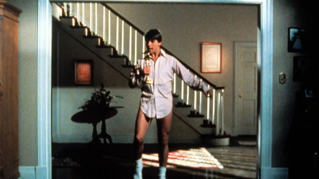 The famous scene from Risky Business showing Tom Cruise dancing in a white dress shirt and underwear in a home interior, sliding across the floor.