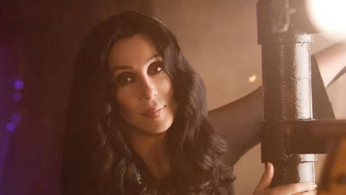 Close-up portrait of Cher with long dark wavy hair in a scene from the movie Burlesque, with soft lighting creating a dramatic effect.