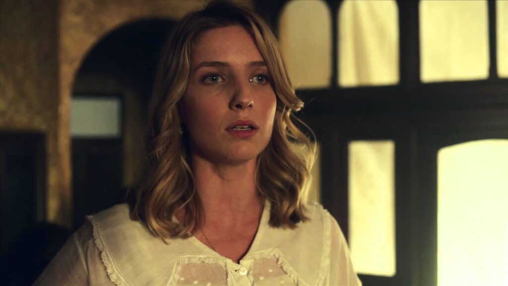 How Many Girlfriends Did Chris Martin Have? Full Relationship History 6 Annabelle Wallis with blonde wavy hair wearing a white lace-collared blouse, photographed in dramatic lighting with windows visible in the background in a still from Peaky Blinders.