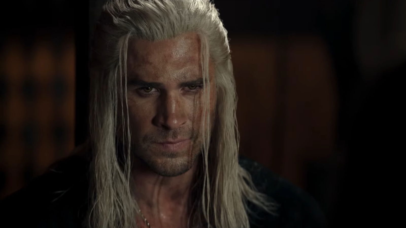 A close-up headshot of Liam Hemsworth as Geralt showing his weathered, battle-hardened appearance with the distinctive white hair and piercing eyes that define the character.