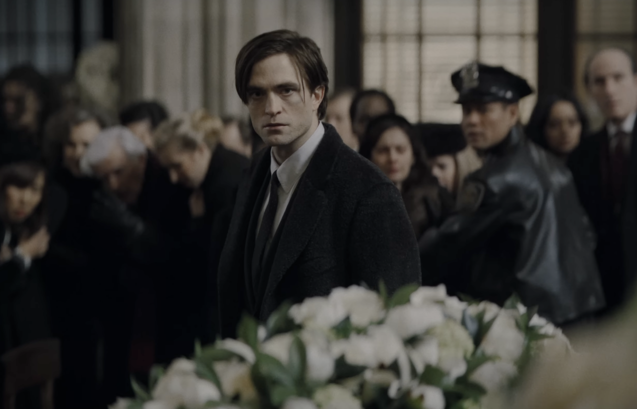 Robert Pattinson como Bruce Wayne, vestido con un traje durante la escena del funeral en The Batman. 