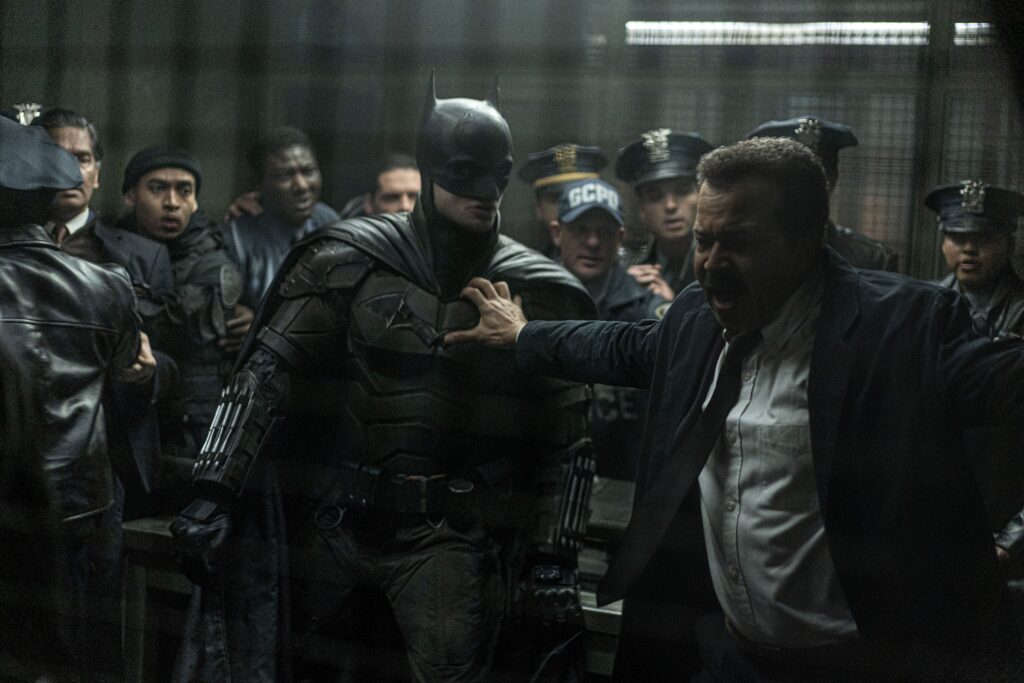 Commissioner James Gordon holding robert pattinson's batman suit with his mouth open with multiple men around them in a still from The Batman