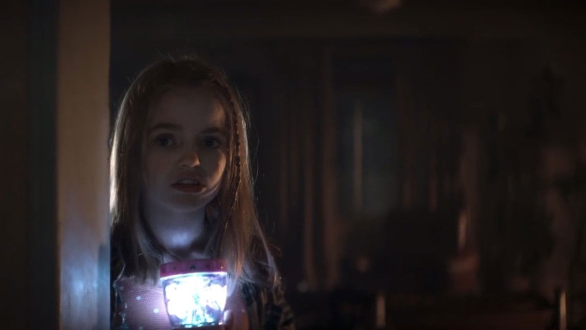 Nell Fisher holding glowing toy in dark room in Evil Dead Rise horror scene