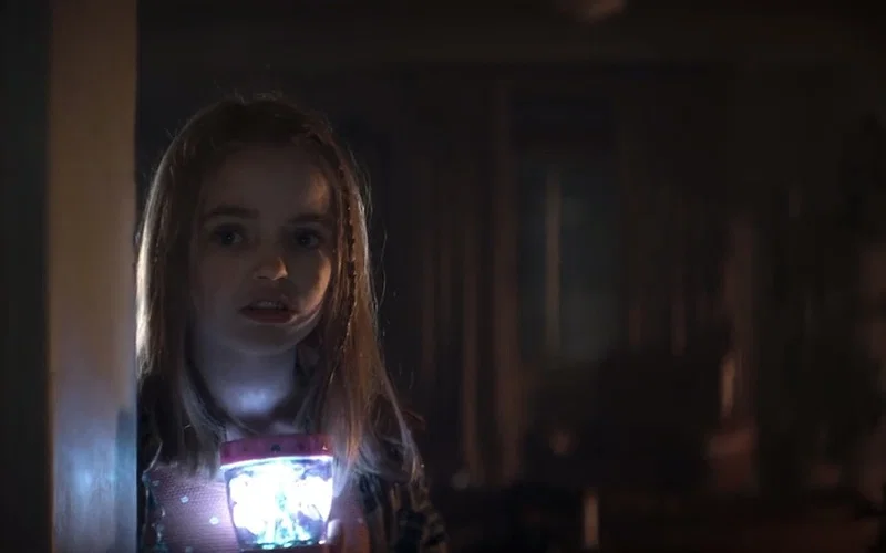 Nell Fisher holding glowing toy in dark room in Evil Dead Rise horror scene