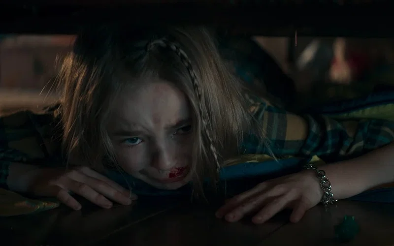 Nell Fisher as Kassie with scared expression hiding under the bed with blood near her nose in Evil Dead Rise