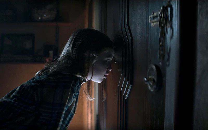 Nell Fisher as Kassie looking through peephole at door in tense Evil Dead Rise scene