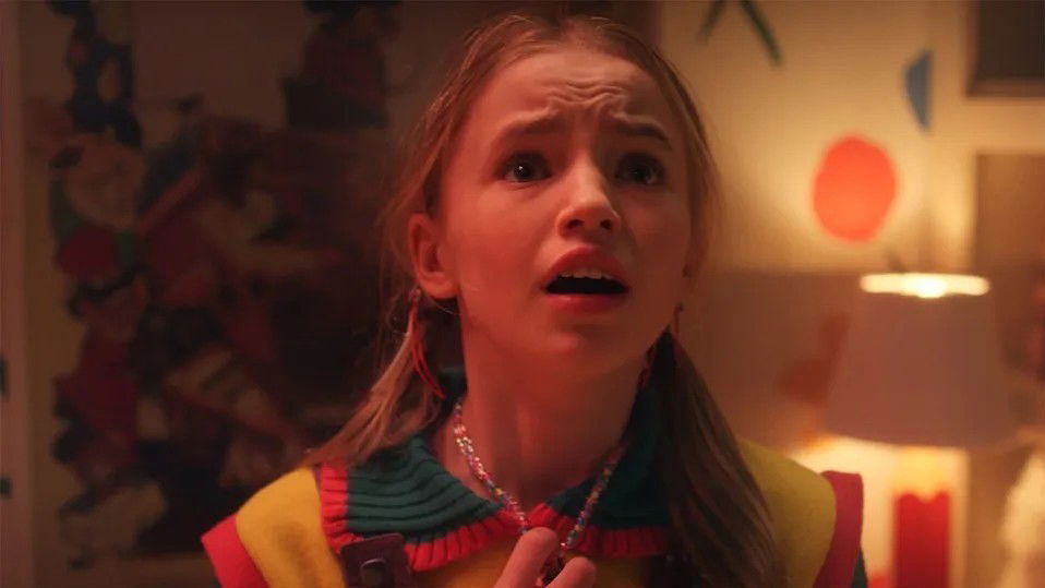 Stranger Things: Who Is Holly Wheeler? Nell Fisher’s Character in Finale Season Decoded 2 Nell Fisher as Holly Wheeler looking worried in Stranger Things wearing a colorful striped shirt in the Wheeler house