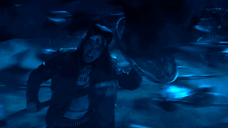 Eddie Munson fighting off the demobats with a makeshift shield and spear in the Upside Down with blue atmospheric lighting in Stranger Things Season 4
