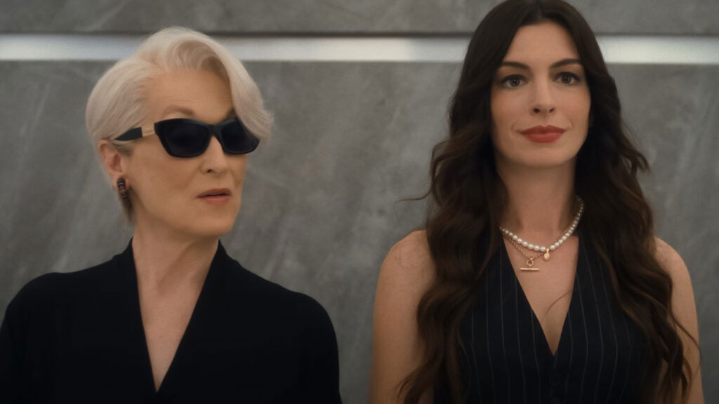 Meryl Streep as Miranda Priestly with sunglasses looking sideways at Anne Hathaway as Andy who is smiling in The Devil Wears Prada 2