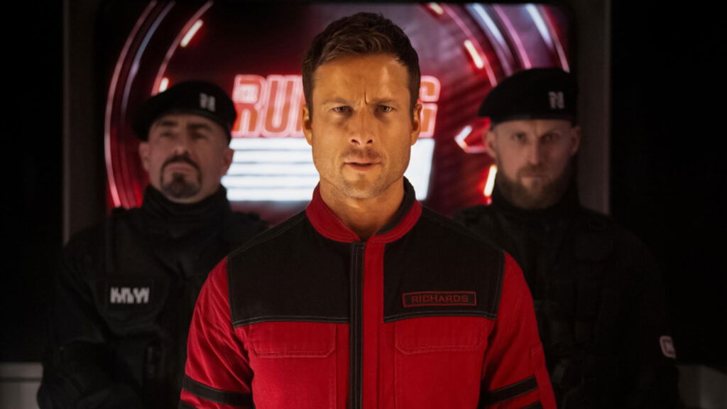 Glen Powell standing in The Running Man.