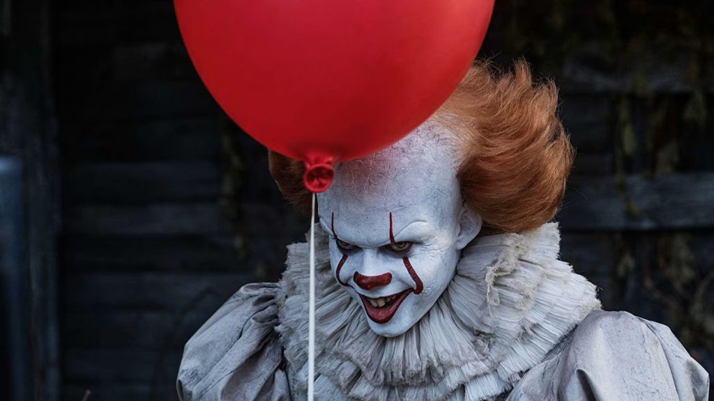 Bill Skarsgård as Pennywise the Dancing Clown from the 2017 movie IT holding a red balloon and smiling menacingly