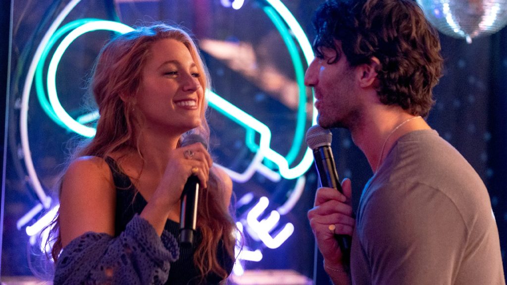 blake lively’s character smiling while holding a mic with justin baldoni's character in It Ends With Us
