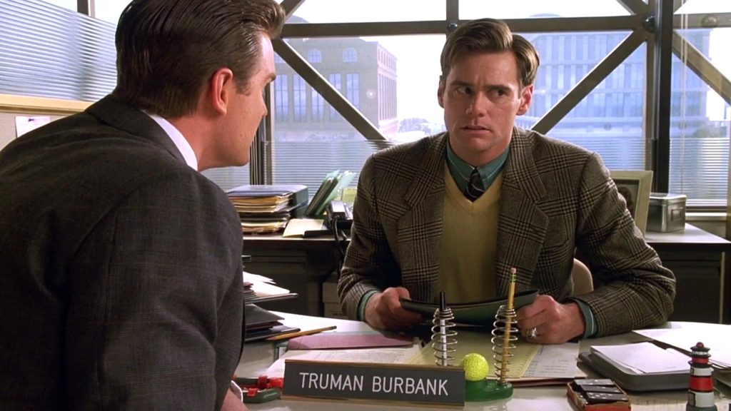 Jim Carrey sitting in an office, wearing a suit 