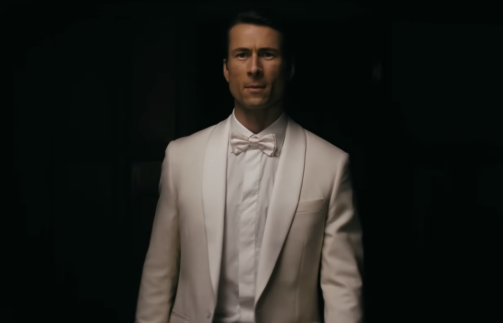Glen Powell wearing a white suit in How to Make a Killing
