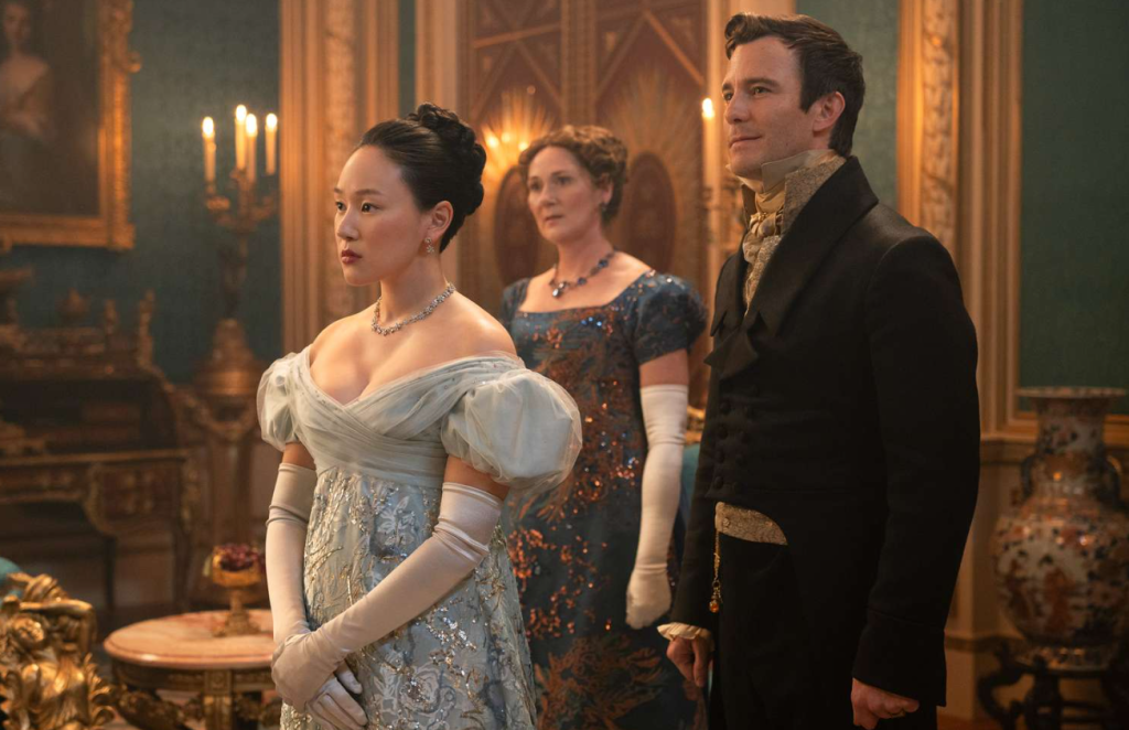 Sophie Baek (Yerin Ha) wearing a strapless eggshell coloured gowk with puffy sleeves and gloves, standing next to Benedict Bridgerton (Luke Thompson) in Bridgerton Season 4 | Credit: Netflix