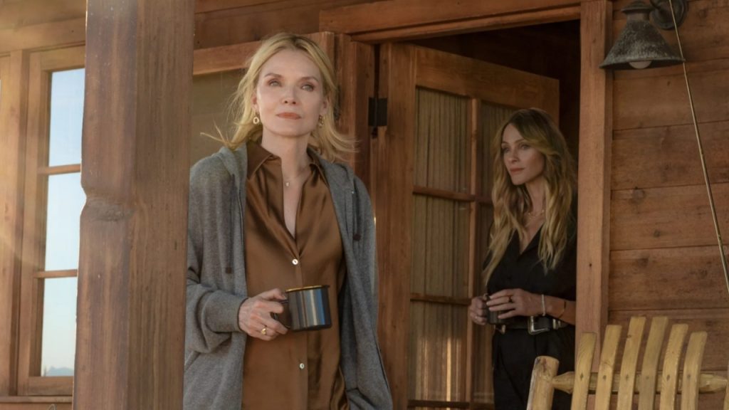 Michelle Pfeiffer holding a coffee mug on a wooden cabin porch alongside another woman in a scene from The Madison on Paramount+

