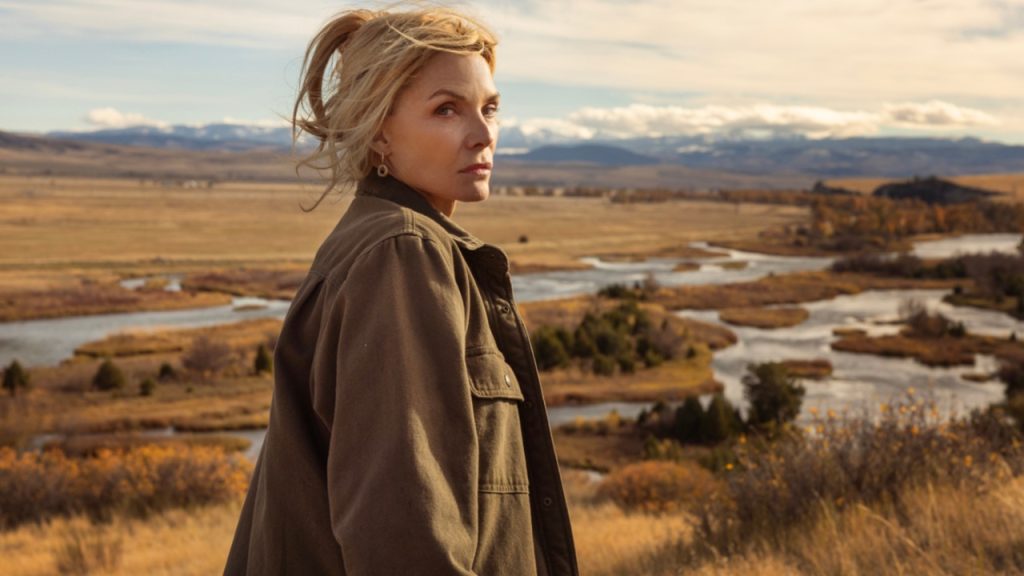 Michelle Pfeiffer as a woman in a khaki coat standing on a hilltop overlooking a vast Montana river valley in The Madison