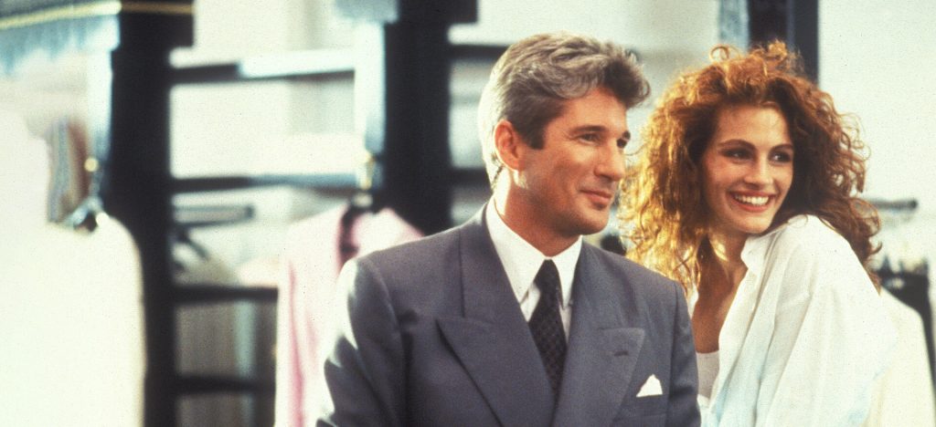 A well-dressed man and a smiling woman stand together with smiles, sharing a light moment.