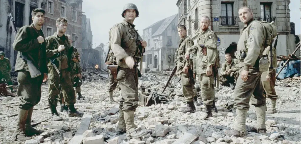 A group of exhausted American soldiers in World War II uniforms stand amid the rubble of a destroyed European town in a scene from Saving Private Ryan.