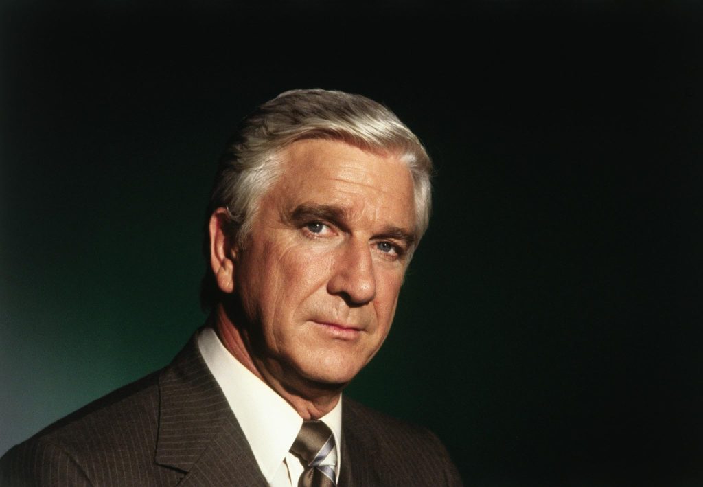 Leslie Nielsen in a suit stares seriously toward the camera against a dark background in a promotional image from Airplane!.