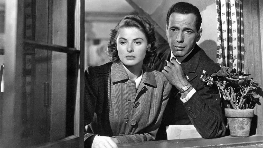 Ingrid Bergman and Humphrey Bogart lean beside a window looking thoughtfully into the distance in a black-and-white scene from Casablanca.