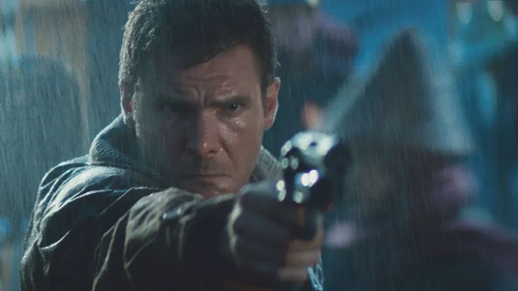 Harrison Ford as Rick Deckard points a gun intensely through heavy rain in a dark neon-lit scene from Blade Runner.