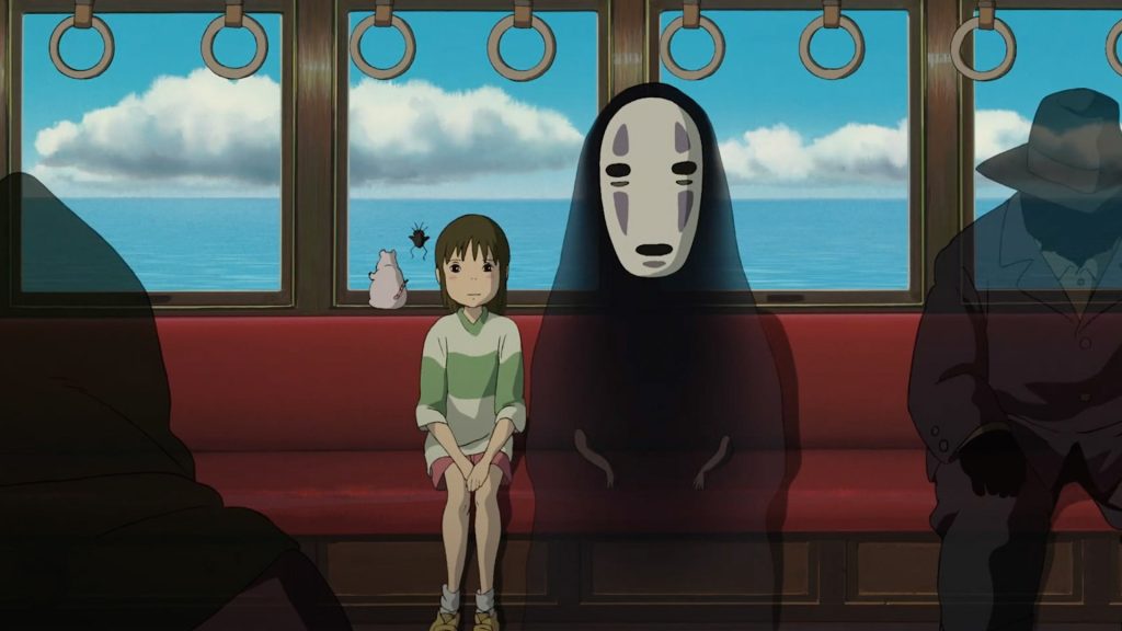 An animated girl sits quietly on a red train seat beside the masked spirit No-Face in a scene from Spirited Away, with the ocean and clouds visible through the windows behind them.