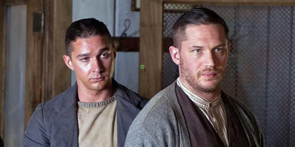 Shia LaBeouf and Tom Hardy as Jack and Forrest Bondurant, in period 1930s clothing, standing together in an interior setting in Lawless (2012)