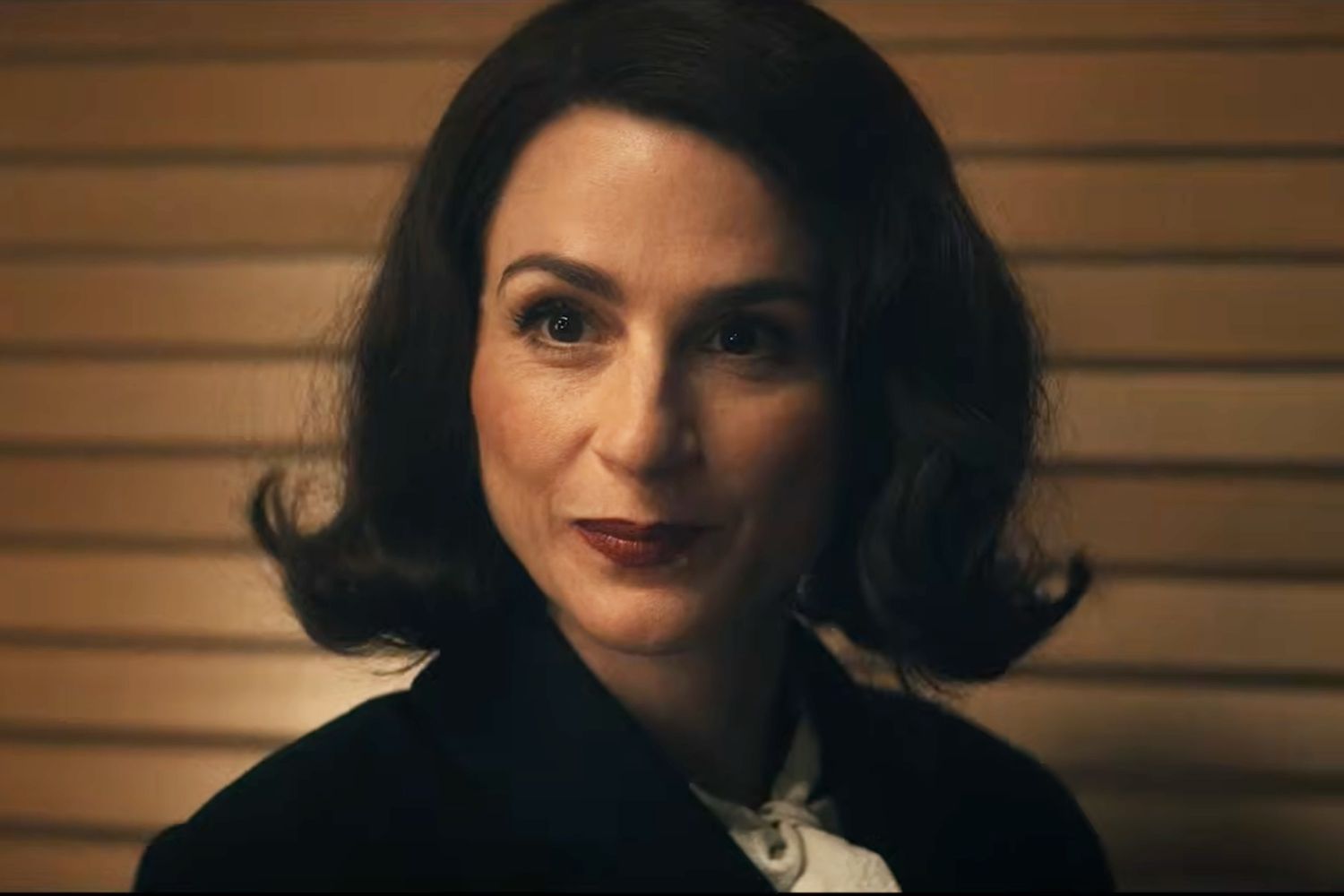 Aya Cash as Clara Vought, dark-haired and wearing 1950s period clothing, smiling subtly in a warmly lit interior in Vought Rising (2027)