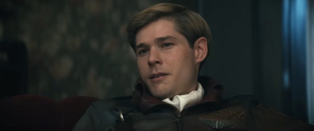 Mason Dye as Bombsight, a young blond man wearing a 1950s-style leather aviator jacket with insignia, in a dimly lit interior in Vought Rising (2027)