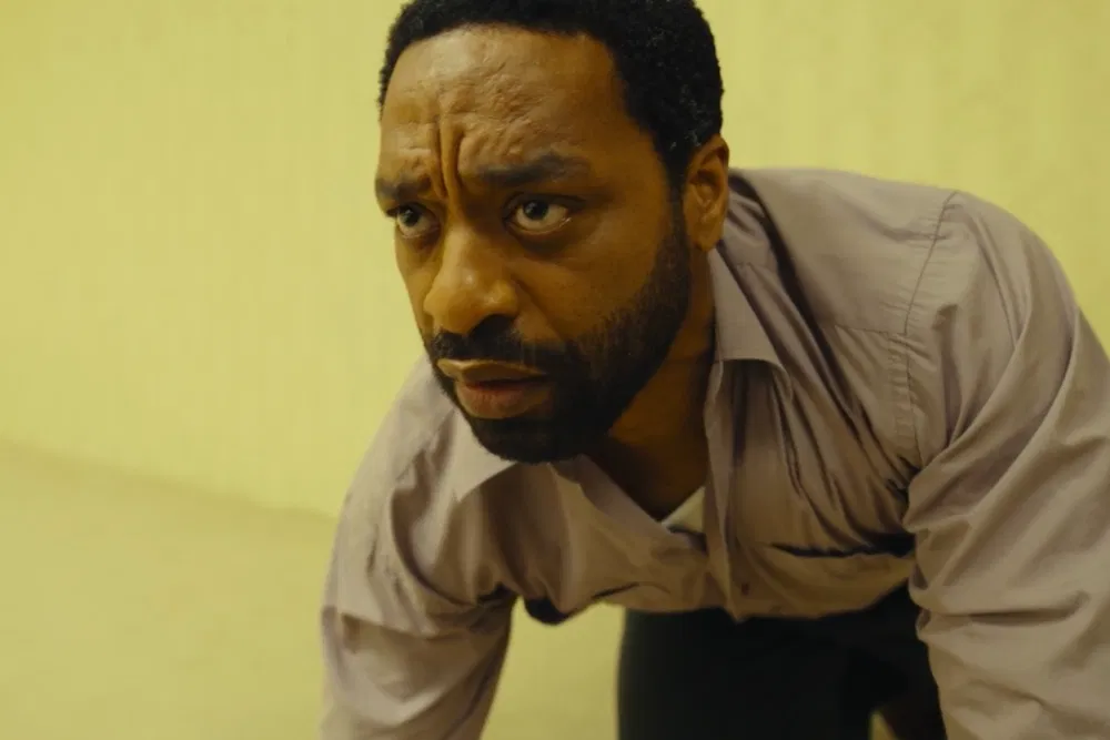 Chiwetel Ejiofor as Clark crouched low against a yellow wall, his expression tense and fearful, deep inside the Backrooms in Backrooms (2026)
