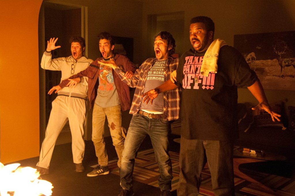 Seth Rogen, Jay Baruchel, Danny McBride, and Craig Robinson screaming in terror as flames erupt on the floor in front of them inside Franco's house.