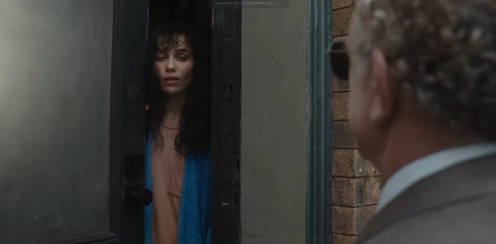 Zoë Kravitz as a hacker under house arrest opening her front door to a suited man, her expression guarded and reluctant.