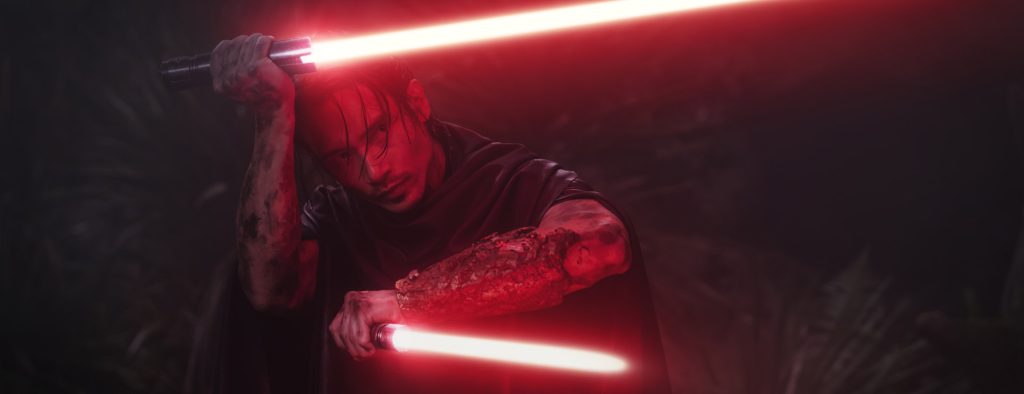 Manny Jacinto as Qimir, the Stranger, wielding two red lightsabers in a darkly lit scene from Star Wars: The Acolyte