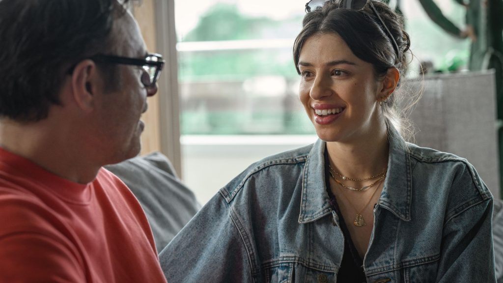 Alice and Steve Season 1 Ending Explained: Did Alice and Steve Survive the Fire? 5 Steve and Izzy in alice and steve sit together on a couch, smiling as they share a conversation in a bright apartment.