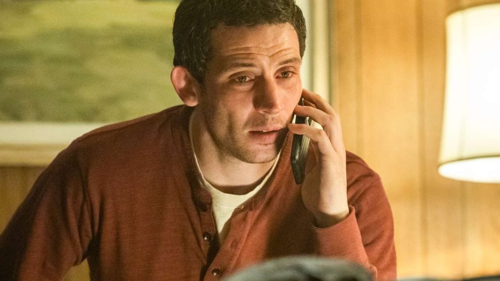 Josh O'Connor as Daniel Kellner in Disclosure Day, on a phone call with a tense, wide-eyed expression, wearing a rust-red henley in a warmly lit room.