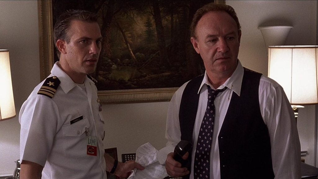 Naval officer Tom Farrell and Defense Secretary David Brice react to a shocking discovery in a tense scene from No Way Out, standing inside a dimly lit office with documents in hand.