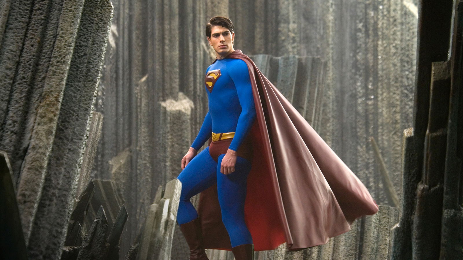 A caped superhero in a bright blue suit stands among towering crystalline structures, his red cape billowing behind him.