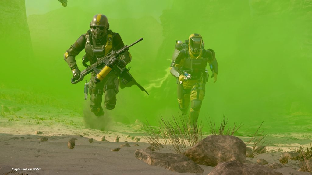 Helldivers 2 screenshot shows two players running out of a cloud of bright green gas on a desert planet.
