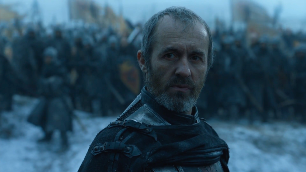 A bearded man in dark armor stands on a snowy battlefield, looking over his shoulder with a stern expression as soldiers gather in the blurred background.