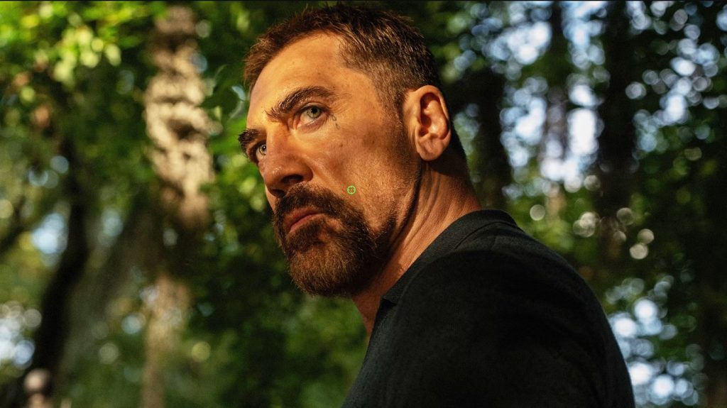 Max Cady looks over his shoulder in a wooded area, his intense expression hinting at the growing danger surrounding the Bowden family