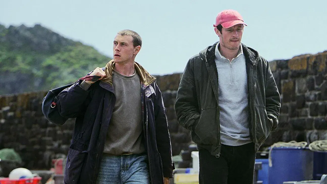 Nick and Liam walk through a Cornish fishing village carrying their belongings, unaware that a trip aboard the Rose of Nevada will transport them to 1993.